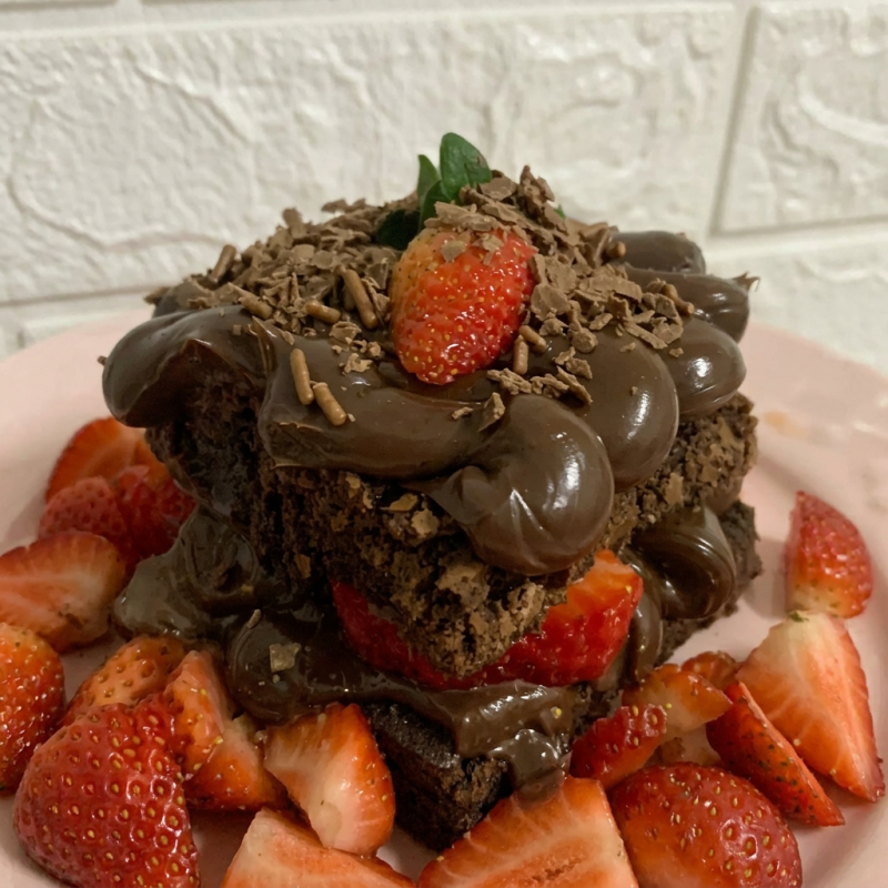 Base de brigadeiro preto com uma fatia generosa de brownie coberto com morango e brigadeiro de chocolate *Foto ilustrativa*