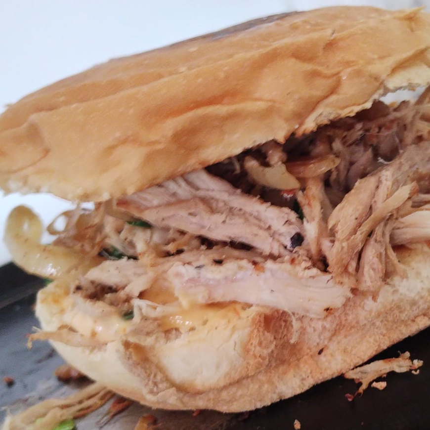 Pão macio recheado com pernil desfiado lentamente, bem temperado e suculento, refogado na chapa com cebola dourada