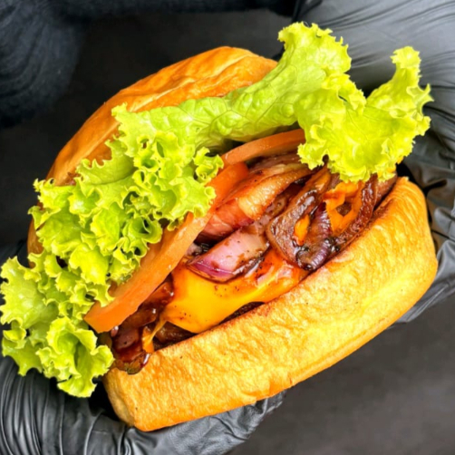 Pão brioche tostado na manteiga, hambúrguer crocante 150 g, queijo cheddar, cebola caramelizada, alface e maionese da casa