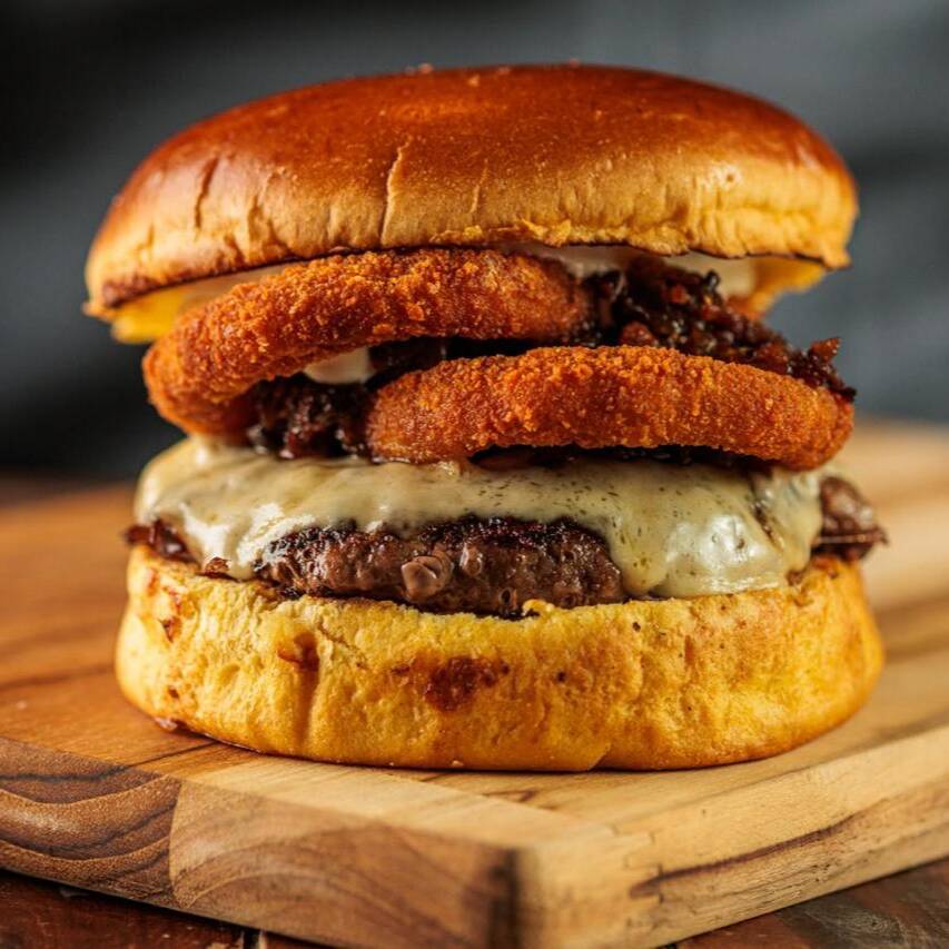 Pão brioche, Blend Angus 160g na brasa, geleia de pimenta, onion rings e queijo cheddar.