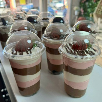 Copo composto por: pedaços de chocolate, camadas intercaladas de mousse de ninho, mousse de chocolate e mousse de morango