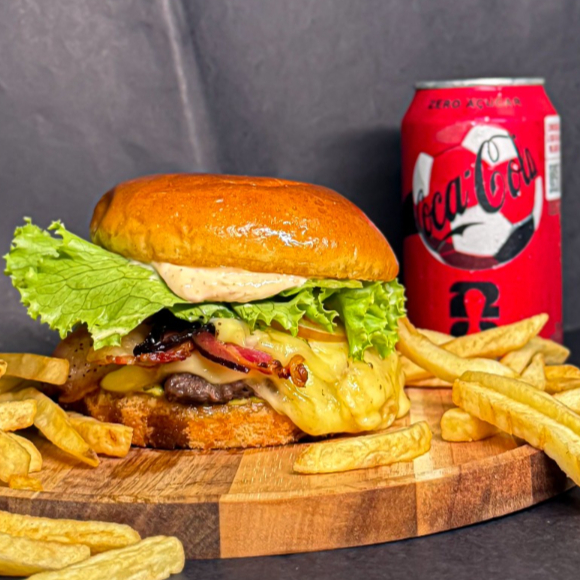 Delicioso hambúrguer artesanal no pão brioche, com blend bovino suculento de 150g, queijo mussarela, queijo coalho na chapa, melaço de cana, bacon crocante, cebola caramelizada, alface e tomate frescos, acompanhado das maioneses especiais da casa. O combo acompanha 150g de batata frita crocante e uma Coca-Cola lata bem gelada.