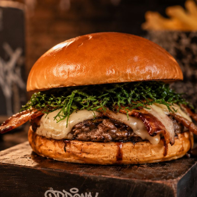 Hambúrguer Angus 150g, queijo mozzarella derretido, bacon crocante, couve crisp, molho tare caramelizado, servido no pão de hambúrguer.