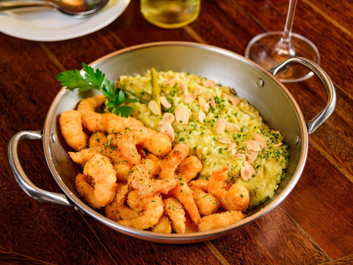 Camarões empanados acompanhados de risoto de aspargos e parmesão coberto com lâminas de amêndoas assadas.
