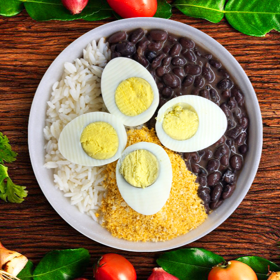 Arroz, Feijão, Farofinha temperada e 2 Ovos Cozidos (Peso total 350g). Atenção: Utilizamos Bacon no tempero do feijão e farofa.