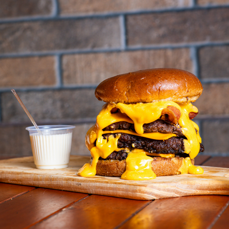 Pão pretzel, 3 smash 90 gr, 3 fatias de cheddar, bacon exagerado, creme de cheddar, maionese da casa . O 'Smash Rei Cheddar', da categoria 'Smash Burguer', é uma obra-prima culinária. Ele consiste em um fascinante pão pretzel, que abriga três saborosos e suculentos smashs de 90g cada, perfeitamente temperados. Acompanhados de três generosas fatias de cheddar autêntico, que derretem maravilhosamente