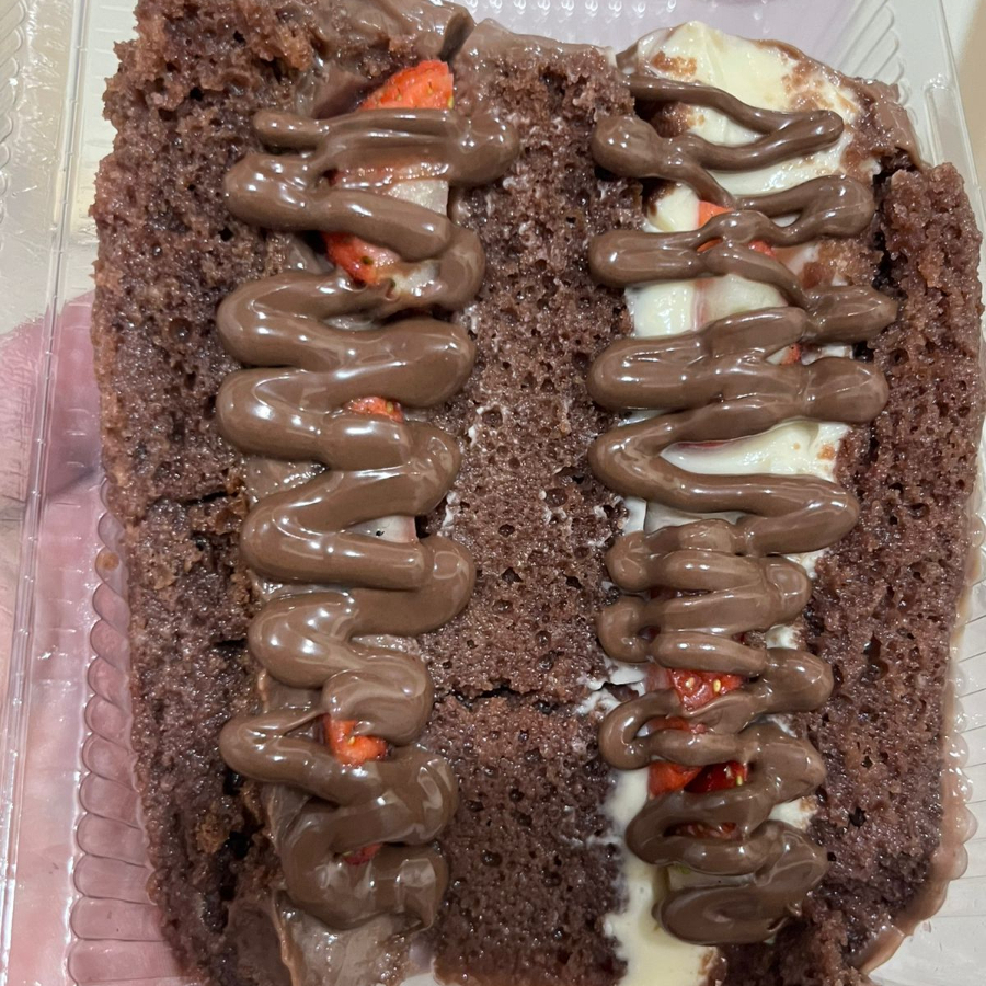 Fatia de massa de chocolate com recheio de chocolate e chocolate branco, finalizada com morangos. Tem opções de calda. Serve 1 pessoa.