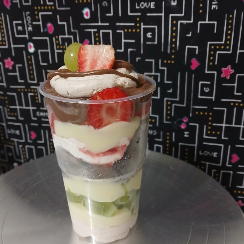 Uma explosão de sabores que abraça seu coração! Camadas generosas de morango e uva fresquinhos, brownie molhadinho mergulhado em creme suave de Galak, toque de chocolate 50% e chantilly trufado.  Doçura e equilíbrio em cada colherada — perfeito pra quem ama frutas, chocolate e felicidade no mesmo copo!