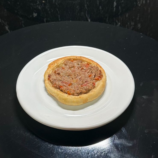Esfiha aberta de carne, feita com receita árabe original e massa artesanal, leve e macia. Recheada com carne moída bem temperada, tomate e um toque especial de limão, é assada no ponto certo, garantindo sabor marcante, suculência e aquele aroma irresistível da culinária árabe. Perfeita para uma refeição deliciosa e autêntica!