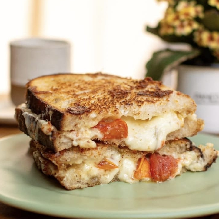 Duas fatias de pão, recheado de muito queijo meia cura e tomatinho confit, selado na chapa.