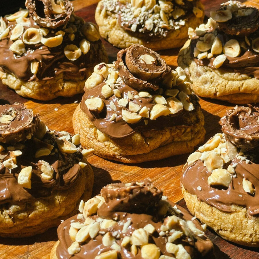 Cookie Ferrero, massa tradicional com gotas de chocolate ao leite, com recheio de chocolate e decorado com Nutella, avelãs e bombom Ferrero o que garante uma experiência incrível de sabores. (Peso medio: 120g a 150g)