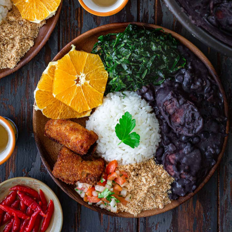 "Feijoada pequena completa, cheia de sabor, acompanhada de arroz soltinho, couve refogada no azeite, torresmo crocante, farofa dourada e vinagrete fresco. Tradição brasileira que conquista no primeiro prato!"