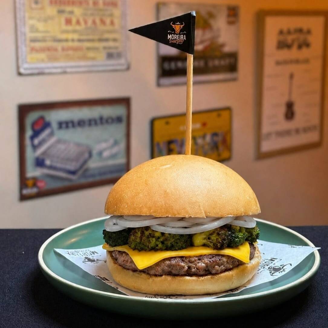 Suculento Burger Angus, Fatias de Queijo Cheddar Americano, Brócolis Selado na Manteiga de Garrafa, Cebola Crua, Maionese, Mostarda. Servido no Pão Levemente Selado