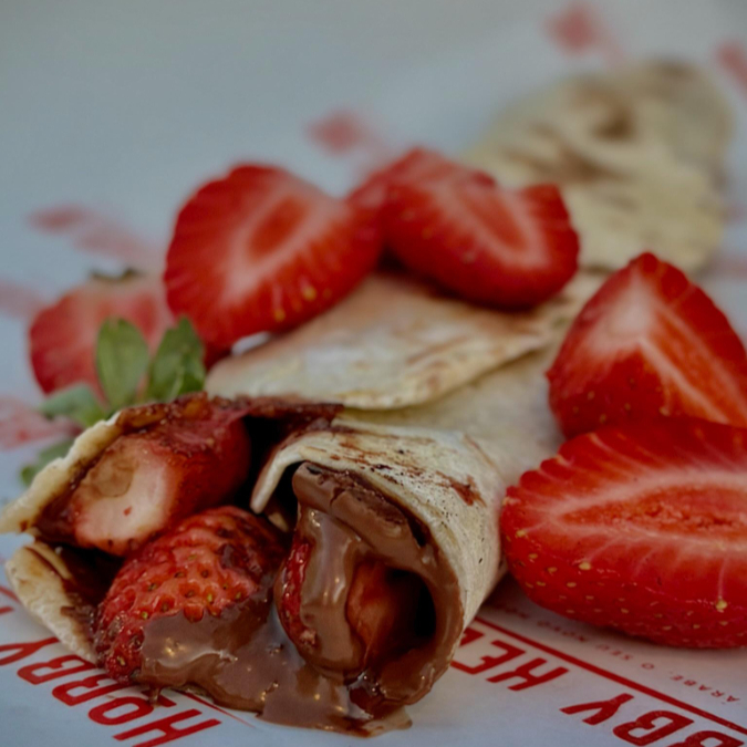 Pão sírio de 25cm recheado com chocolate ao leite e pedaços de morango, criado uma sobremesa única e deliciosa.