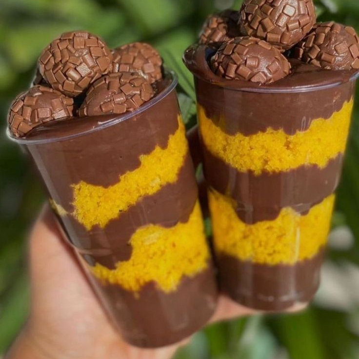 Copo da felicidade com camadas de bolo de cenoura, recheio cremoso de chocolate ao leite 50% cacau e brigadeiros por cima.