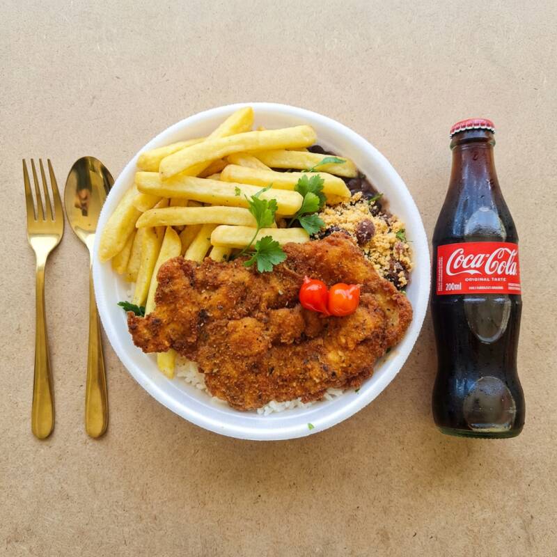 O prato é composto por empanado crocante, acompanhada de arroz soltinho, feijão carioca, batatas fritas crocantes e uma farofa temperada, oferecendo uma refeição saborosa e cheia de personalidade. Uma combinação simples, mas irresistível.