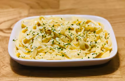 Acompanhamento de fettuccine ao molho alfredo com queijo parmesão. Porção individual.