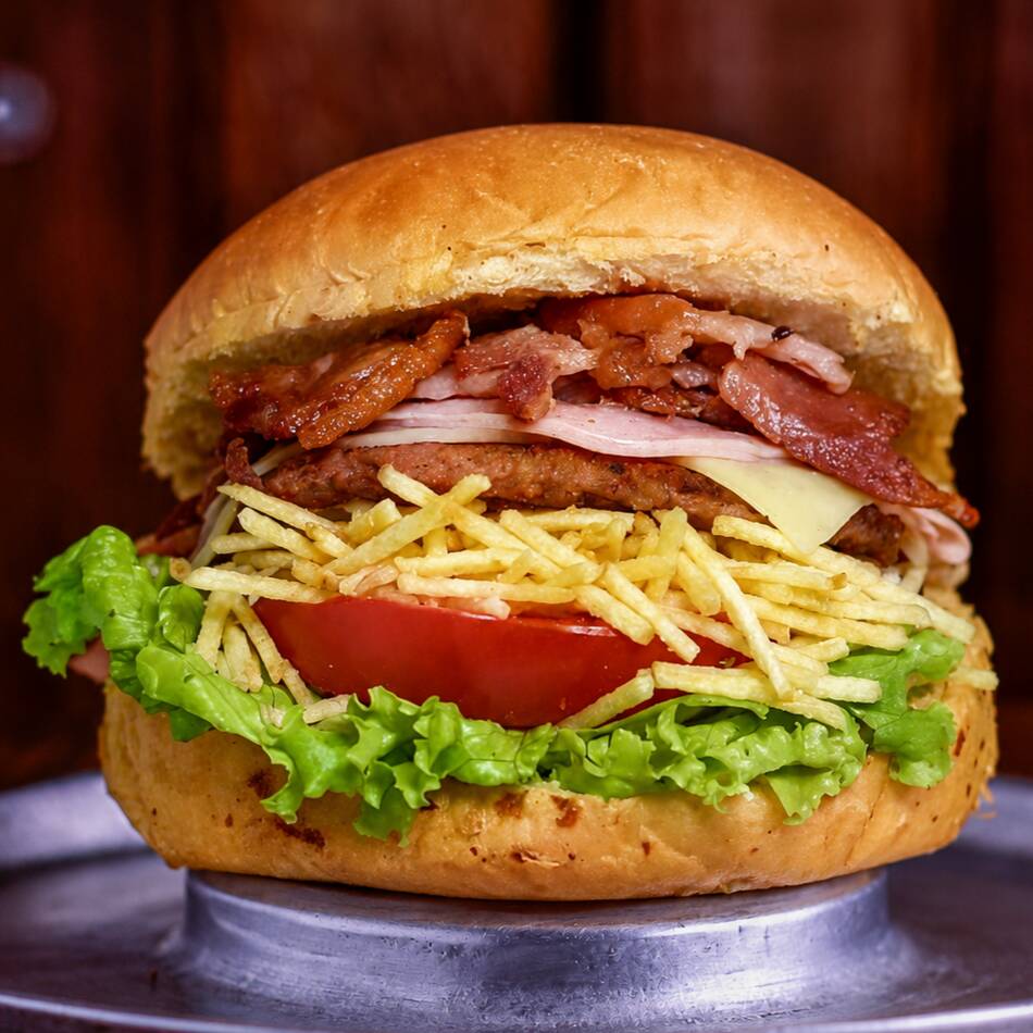 Pão macio com hambúrguer de 100g, muçarela derretida, bacon crocante, Catupiry cremoso, alface, tomate, milho verde e batata palha. Uma combinação completa e irresistível.