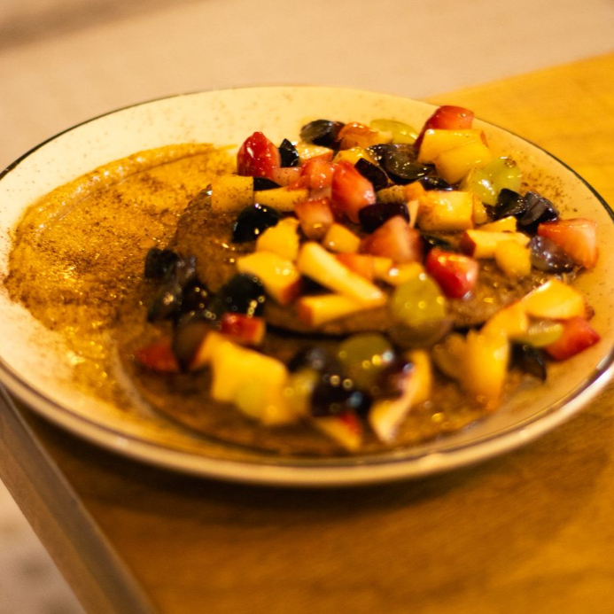 Panqueca feita com banana, ovo, farelo de aveia, nozes, cumaru e canela. Finalizada com frutas frescas do dia, mel e pasta de amendoim da casa.