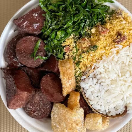 Marmitex de feijoada com feijão preto, carne suína, calabresa e bacon. Acompanha arroz branco, farofa, couve e torresmo crocante.