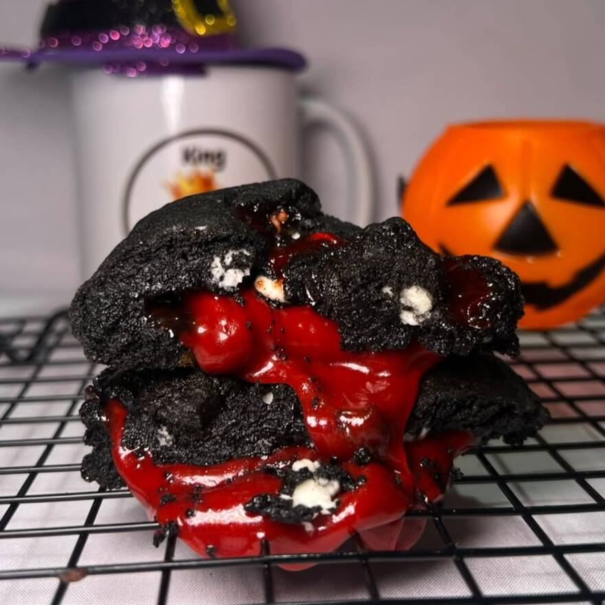 🕸️ Uma massa de cacau black intensa, recheada com gotas de chocolate branco e um irresistível caramelo salgado vermelho-sangue, que surpreende a cada mordida. ❤️🔥