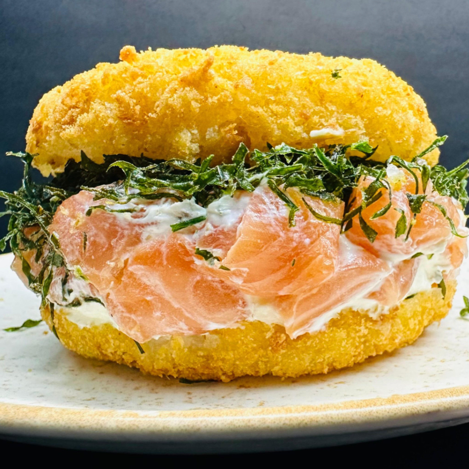 Delicioso arroz temperado empanado cortado ao meio, pedaços de salmão, couve crispy, cebola roxa fatiada, cream cheese e cebolinha pra finalizar.