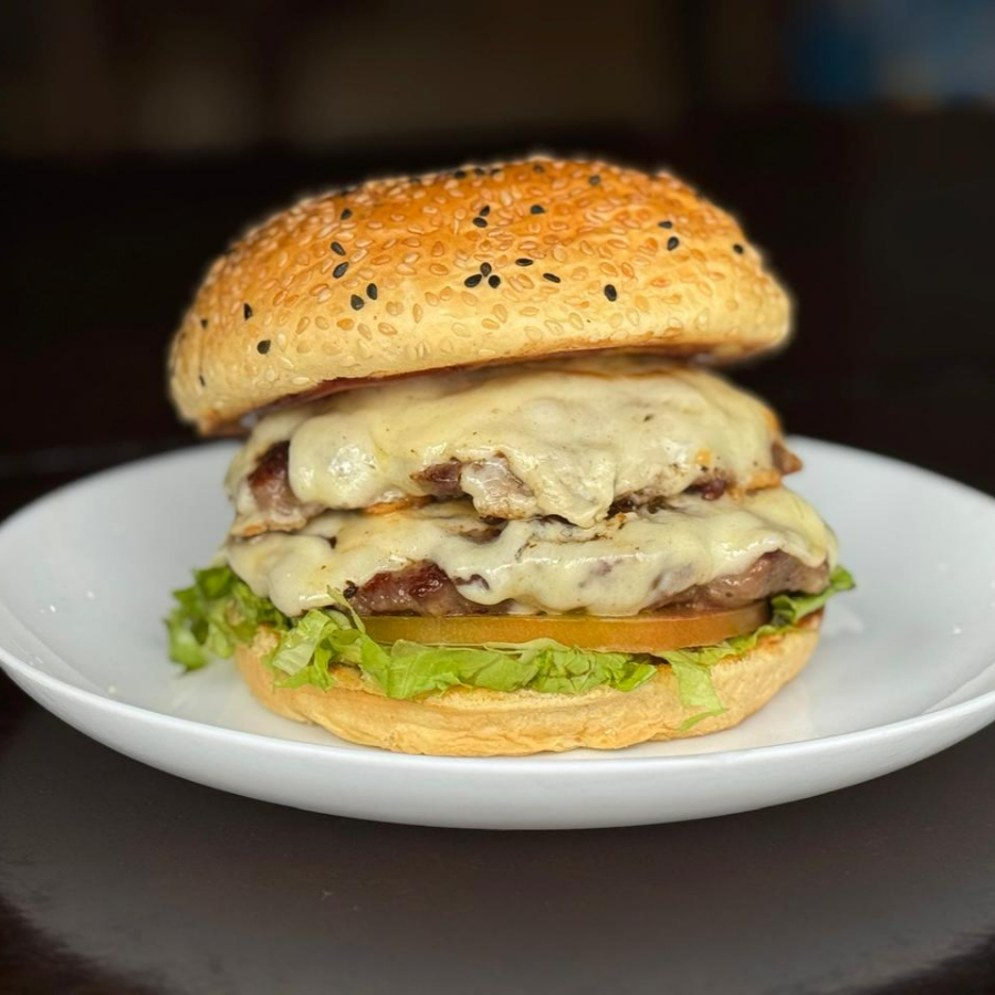Delicie-se com nosso irresistível X-Burguer Duplo, uma criação gastronômica da categoria 'Hambúrgueres'. Este prato é uma generosa combinação de dois suculentos hambúrgueres bovinos, cuidadosamente grelhados para garantir um sabor inigualável. Para complementar, incluímos duas fatias de mussarela derretida, que conferem uma cremosidade irresistível ao sanduíche. O toque especial fica por conta do nosso molho barbecue, que traz um sabor defumado e adocicado, equilibrando perfeitamente os sabores. E para finalizar, uma camada crocante de alface fresca e fatias de tomate suculento, garantindo uma explosão de frescor. Tudo isso acomodado em um pão brioche macio e levemente adocicado. Experimente e se apaixone!