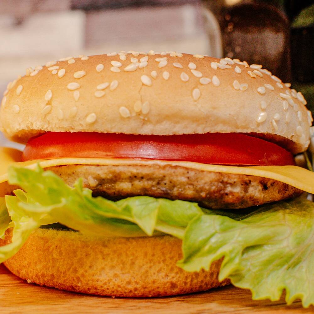 Pão com gergelim, carne bovina de 56g, queijo prato, alface americana e tomate