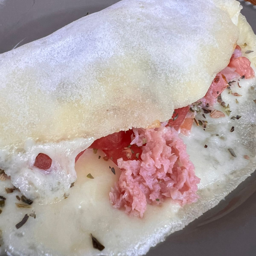 Massa de tapioca feita na casa, mussarela, tomate, presunto e orégano.