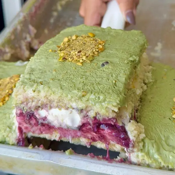 Massa branca molhadinha, recheada com mousse de limão, geleia de frutas vermelhas e Creme de Ninho, finalizada com um irresistível creme de pistache e farelo crocante de pistache.