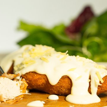 Bife de filé de frango empanado ao molho branco por cima, finalizado com  uma cobertura de queijo mussarela derretido.  Marmita composta por arroz branco, feijão preto, farofa da casa, mais um acompanhamento a escolher.