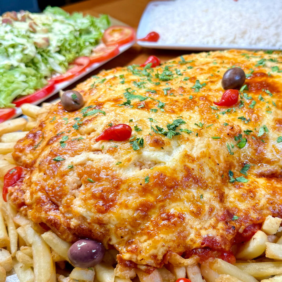 Baby Beef empanado servido ao Molho Vermelho Artesanal e mussarela e gratinado com parmessão. Servido com arroz branco, batatas fritas e salada do Cheff. Serve 5 pessoas