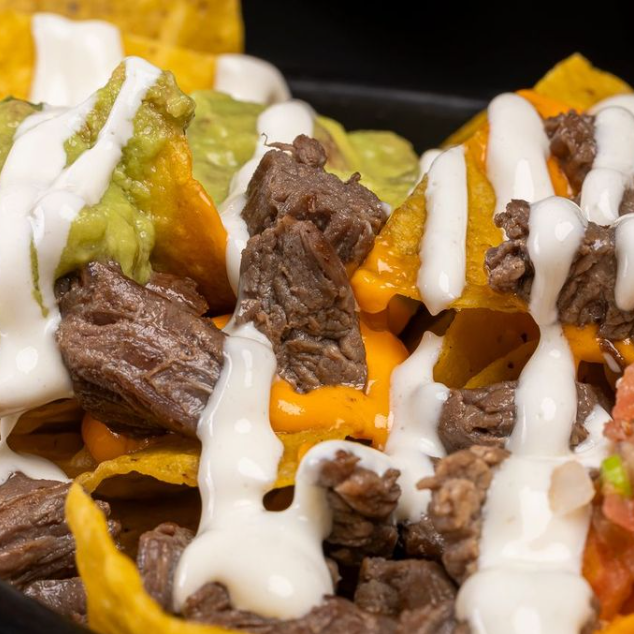 Tortilla chips de milho frita, carne asada, guaca, cheddar, pico de gallo e sour cream