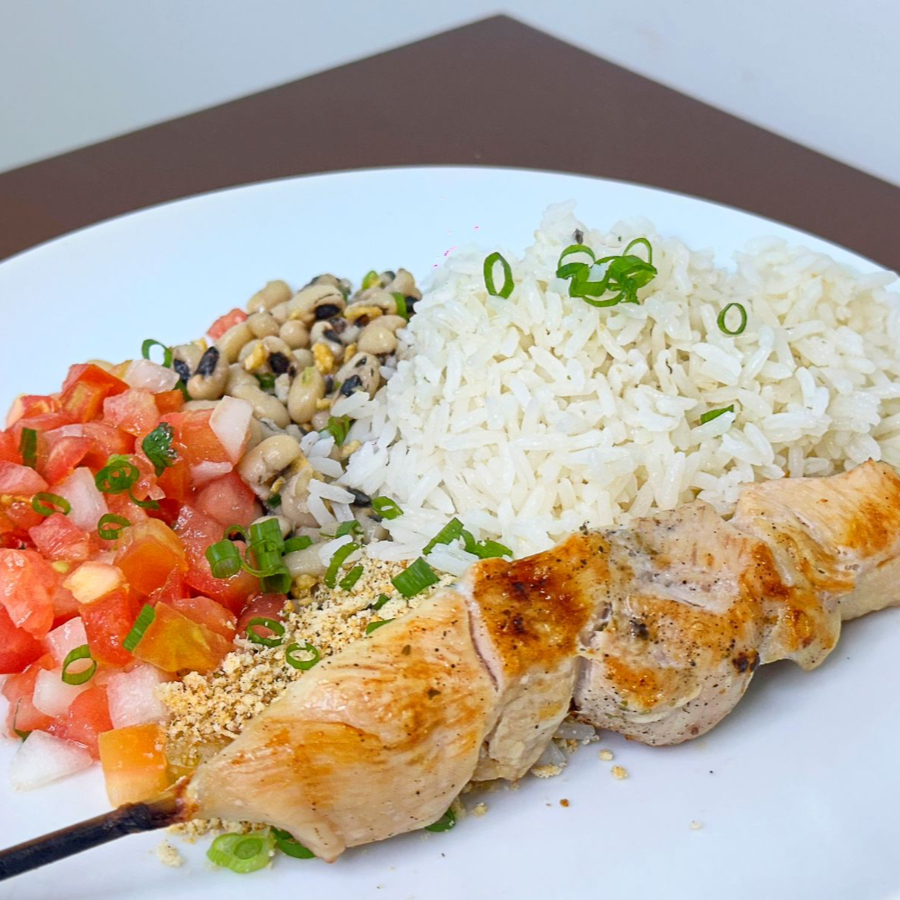 Deliciosa combinação contendo um espeto de frango acompanhado de arroz, feijão fradinho, vinagrete e farofa.