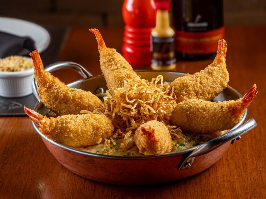 Camarões recheados com Catupiry e empanados. Servidos sobre cremoso arroz com camarões, ervilhas e presunto, envolvido com molho branco. Gratinado com queijos muçarela e parmesão. Acompanha batata palha.