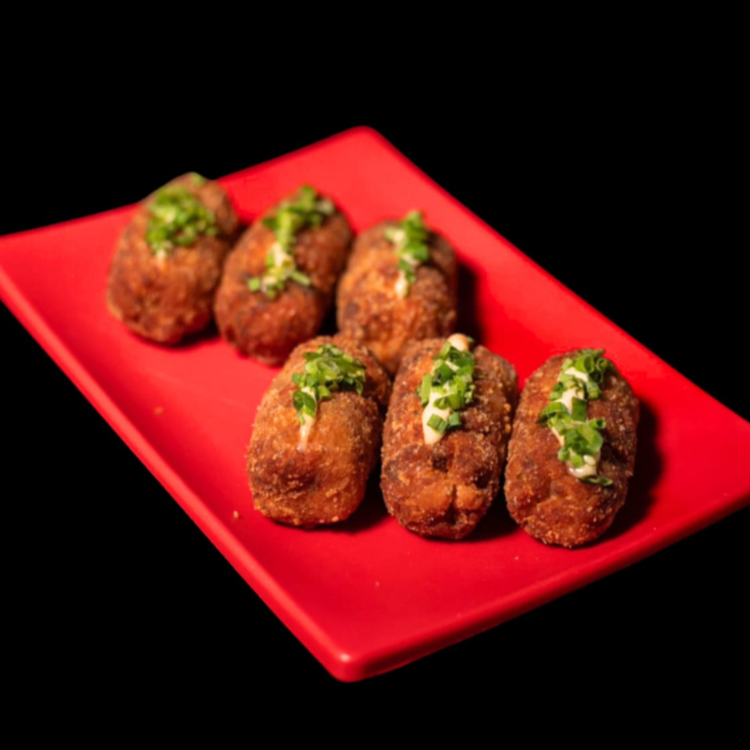 Bolinho de salmão frito, com molho e cebolinha por cima. A porção deste item acompanha 1 molho teriyaki / tarê (30ml)