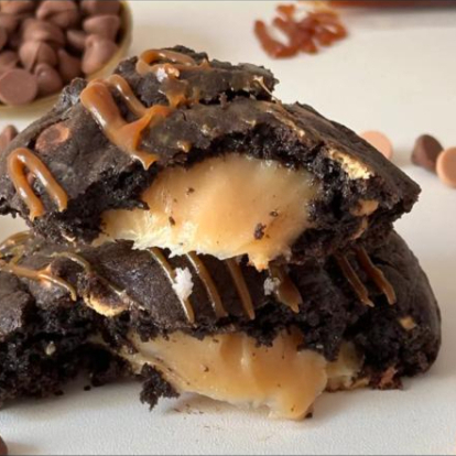 Cookie macio por fora e levemente crocante nas bordas esconde um recheio cremoso de brigadeiro de caramelo salgado, que une o doce do caramelo com um toque sutil de sal, equilibrando perfeitamente os sabores.