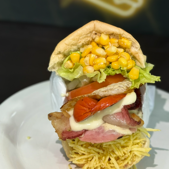 Pão, hambúrguer, salsicha, mussarela, presunto, ovo, bacon, alface, tomate, abacaxi, milho e batata.