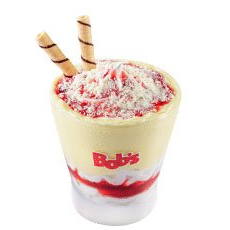 Creme de leite em pó espatulado nas bordas e paredes do copo, mix baunilha coberto de calda com pedaços de morango, finalizado com uma chuva de leite em pó e dois tubetes crocantes.